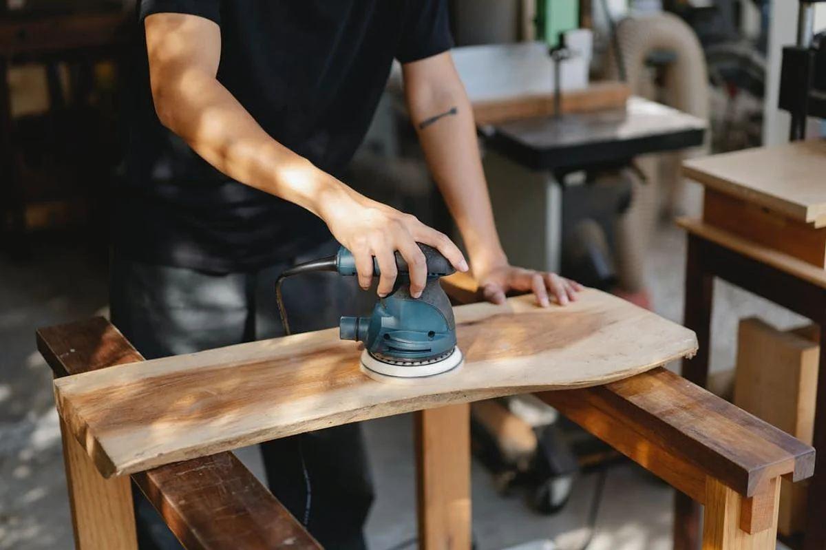 Craftsperson sanding a live-edge wooden tabletop in a furniture workshop